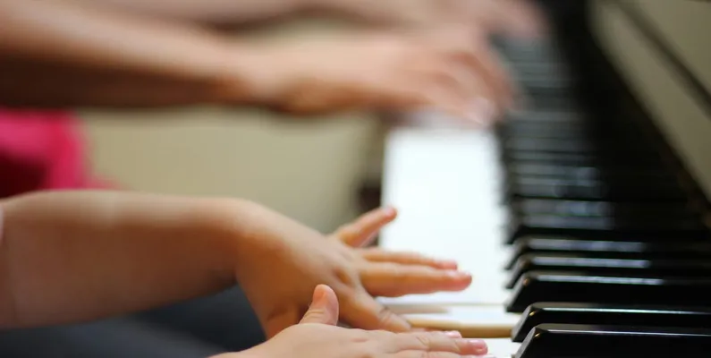 Kinderhände und Erwachsenenhände nebeneinander auf den Tasten eines Klaviers